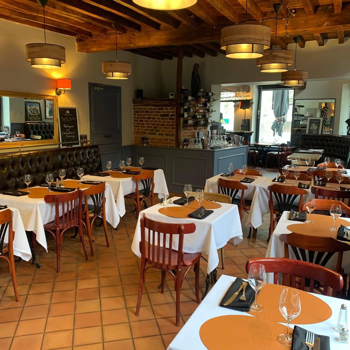La salle du bistrot : poutres apparentes, banquettes, nappes blanches et suspensions